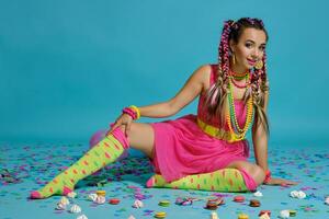 encantador niña con un multicolor trenzas peinado y brillante constituir, posando en estudio con aire globos y papel picado en contra un azul antecedentes. foto