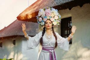 Brunette girl in a white ukrainian authentic national costume and a wreath of flowers is posing against a white hut. Close-up. photo