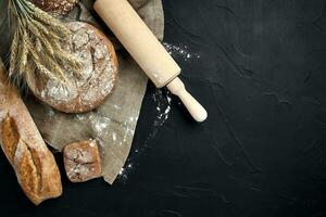 Top view of baguette, baked bread, flour and wheat spikes composition with wheat flour sprinkled around on a dark background photo