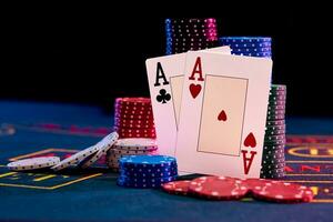 Two aces standing leaning on chips piles, some of them are laying nearby on blue cover of playing table. Black background. Casino concept. Close-up. photo