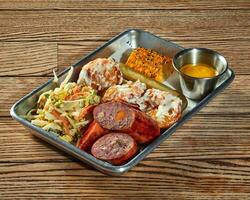 Lunch set of sausage, potato croquettes with creamy dressing, vegetable salad, pickles and grilled corn photo