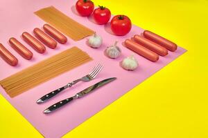 A lot of raw sausages with pasta and vegetables on pink and yellow background, top view. photo