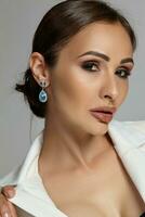 Close up portrait of a brunette model girl with professional evening make-up, wearing a white jacket with black bra, posing on gray background. photo