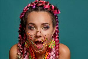 encantador niña con un multicolor trenzas peinado y brillante constituir, posando en estudio en contra un azul antecedentes. vistoso Adición es en su rostro. foto