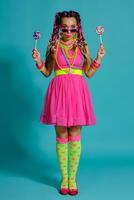 Lovely girl with a multi-colored braids hairstyle and bright make-up, posing in studio against a blue background, holding a lollipop in her hand. photo