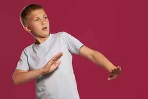 Close-up portrait of a blonde teenage boy in a white t-shirt posing against a pink studio background. Concept of sincere emotions. photo