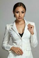 Close up portrait of a brunette model girl with professional evening make-up, wearing a white jacket with black bra, posing on gray background. photo