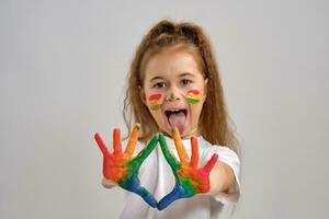 Little girl in white t-shirt is posing standing isolated on white and gesticulating with her painted in different colors palms. Art studio. Close-up. photo