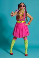 Lovely girl with a multi-colored braids hairstyle and bright make-up, posing in studio against a blue background, holding a lollipop in her hand. photo