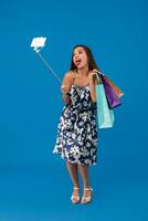 Young stylish woman posing and taking a selfie on the phone with shopping bags on a blue background photo