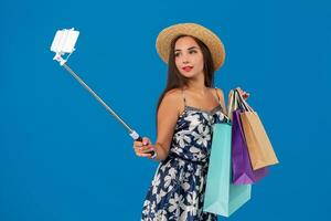 Young stylish woman posing and taking a selfie on the phone with shopping bags on a blue background photo