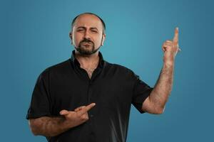 Close-up portrait of a brunet middle-aged man with beard, dressed in a black t-shirt and posing against a blue background. photo