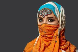 Studio shot of a chrming female wearing the colorful hijab decorated with sequins and jewelry. Arabic style. photo