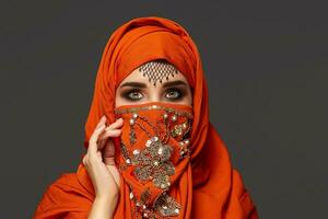 Studio shot of a young charming woman wearing the terracotta hijab decorated with sequins and jewelry. Arabic style. photo