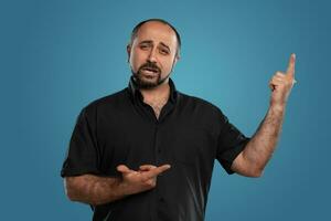 Close-up portrait of a brunet middle-aged man with beard, dressed in a black t-shirt and posing against a blue background. photo