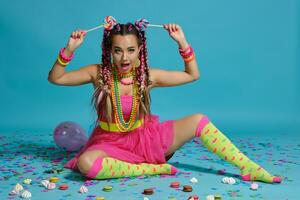 encantador niña con un multicolor trenzas peinado y brillante constituir, posando en estudio con chupete, aire globos y papel picado en contra un azul antecedentes. foto