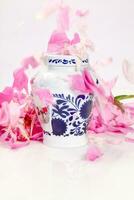 Decorative jar with blue floral patterns sprinkled with pink peony petals photo