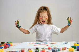 pequeño niña en blanco camiseta sentado a mesa con qué hombre y pinturas en él, posando con pintado cara y manos. aislado en blanco. medio de cerca. foto