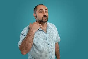 Close-up portrait of a brunet middle-aged man with beard, dressed in a light checkered shirt and posing against a blue background. photo