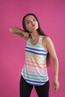 Brunette woman with long hair, dressed in colorful striped shirt, posing against pink studio background. Sincere emotions. Close-up. photo