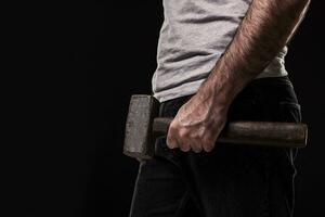 Male offender with a big hammer. On black background at the studio photo