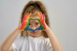 Little girl in white t-shirt is posing standing isolated on white and gesticulating with her painted in different colors palms. Art studio. Close-up. photo