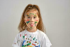 Little girl in white t-shirt, with painted face is making grimaces while posing isolated on white. Art studio. Close-up. photo