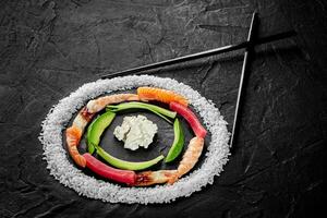 Circle of rice, salmon, eel, tuna and shrimps, avocado and cream cheese with chopsticks on black background photo