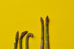 crudo verde espárragos lanzas en amarillo antecedentes. sano nutrición, comida y estacional vegetales cosecha. cerca arriba, plano poner, parte superior ver foto
