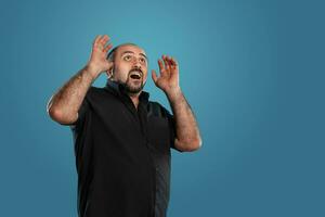 Close-up portrait of a brunet middle-aged man with beard, dressed in a black t-shirt and posing against a blue background. photo