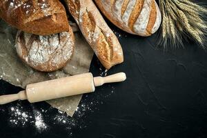 Top view of baguette, baked bread, flour and wheat spikes composition with wheat flour sprinkled around on a dark background photo