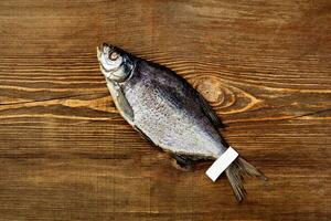 Top view of salted jerked roach fish with label on tail on wooden background photo