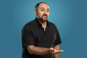 Close-up portrait of a brunet middle-aged man with beard, dressed in a black t-shirt and posing against a blue background. photo