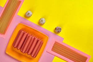 Sausages with spaghetti and garlic on a yellow and pink minimal background. Flat lay. Top view. photo