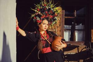 morena niña en un negro y rojo ucranio bordado auténtico nacional disfraz y un guirnalda de flores es posando en pie a el puerta. foto