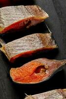 Sices of salted air-dried roach with roe on black wooden surface photo
