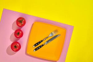 Empty orange plate on a yellow and pink table with red ripe cherry tomatoes, top view with copy space photo