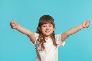 Beautiful little girl wearing in a white t-shirt is posing against a blue studio background. photo