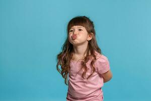 Beautiful little girl wearing in a pink t-shirt is posing against a blue studio background. photo