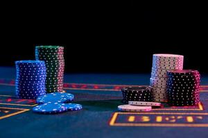 Colorful chips piles standing on blue cover of playing table. Black background. Gambling entertainment, poker, casino concept. Close-up. photo