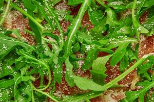 Closeup of arugula leaves on prosciutto slices sprinkled with grated parmesan on pizza photo