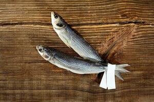 Two air-dried mullets with paper label on tails on wooden surface photo