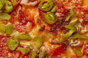 Closeup of pieces of jalapeno peppers on spicy pepperoni pizza photo