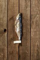 Salted air-dried Baltic herring with label on tail on rough wooden background photo