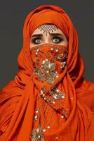Studio shot of a young charming woman wearing the terracotta hijab decorated with sequins and jewelry. Arabic style. photo