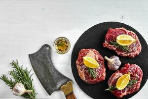 Fresh raw beef steaks with herbs, garlic, olive oil, pepper, salt and rosemary on black board Tenderloin, Striploin, Rib Eye photo