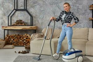 Young smiling woman vacuum cleaning the carpet in the living room, modern scandinavian interior. Home, housekeeping concept photo
