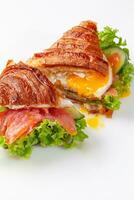 Croissant sandwich cut in half with fried egg, salted salmon, fresh lettuce and cucumber photo