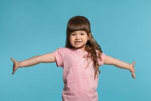 Beautiful little girl wearing in a pink t-shirt is posing against a blue studio background. photo