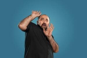 Close-up portrait of a brunet middle-aged man with beard, dressed in a black t-shirt and posing against a blue background. photo